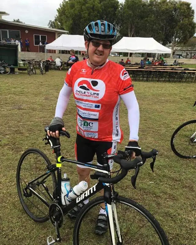 Person in white arm sleeves and a cycling helmet holding a bicycle.