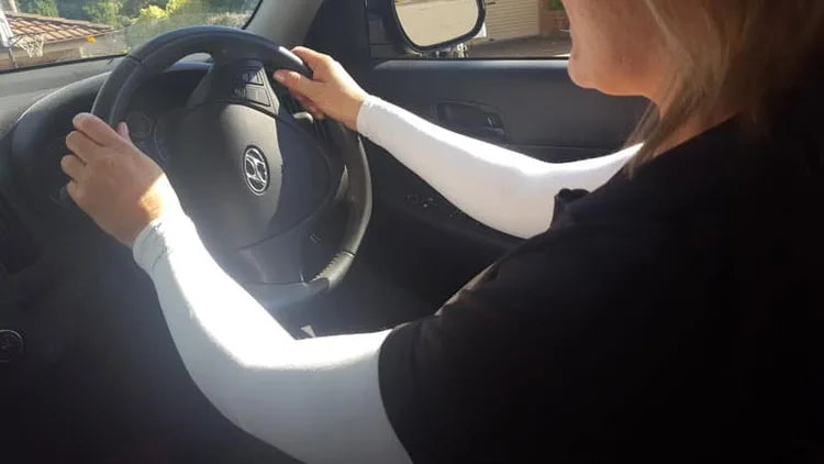 White arm sleeves worn with hands on a car steering wheel.