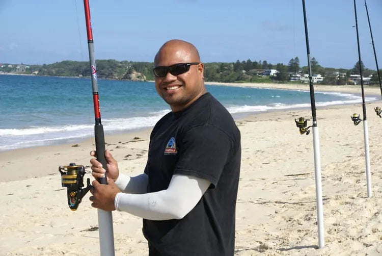 Fisher in white arm sleeves holding a rod at the beach.