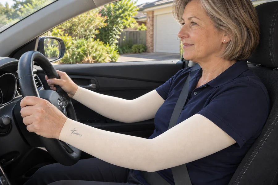 Woman wearing beige IceRays arm sleeves with both hands on the wheel of a parked right-hand-drive car.