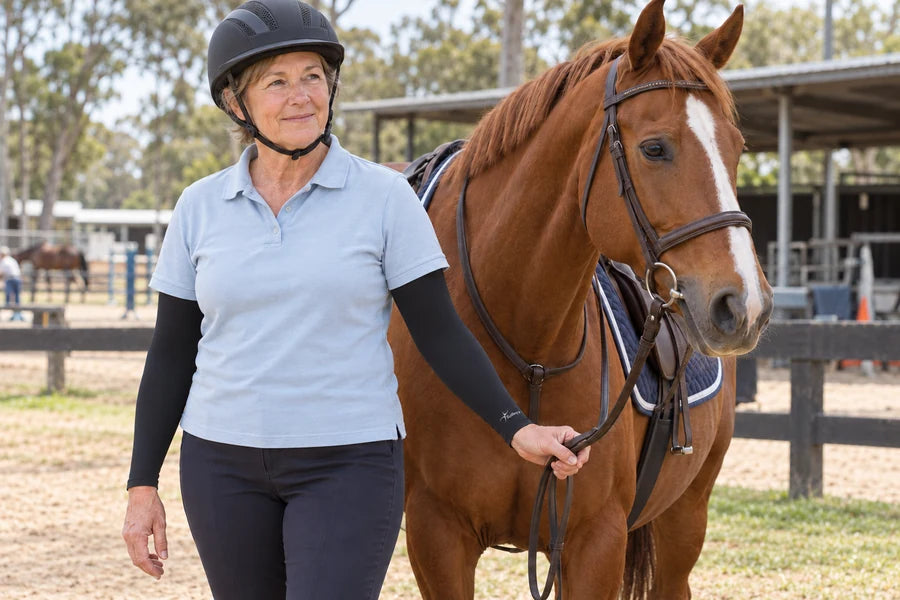 Woman wearing a riding helmet and black IceRays arm sleeves beside a horse.