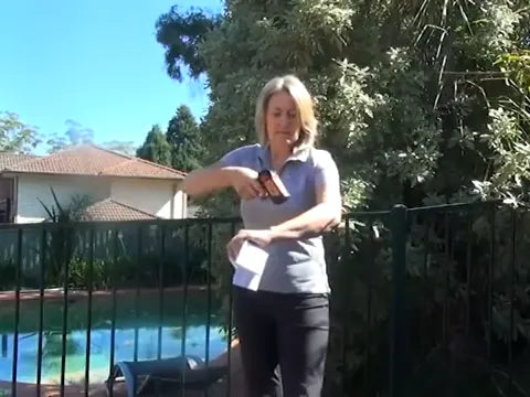 Anne Rollo aiming a handheld thermometer at her bare forearm in a sunny garden.