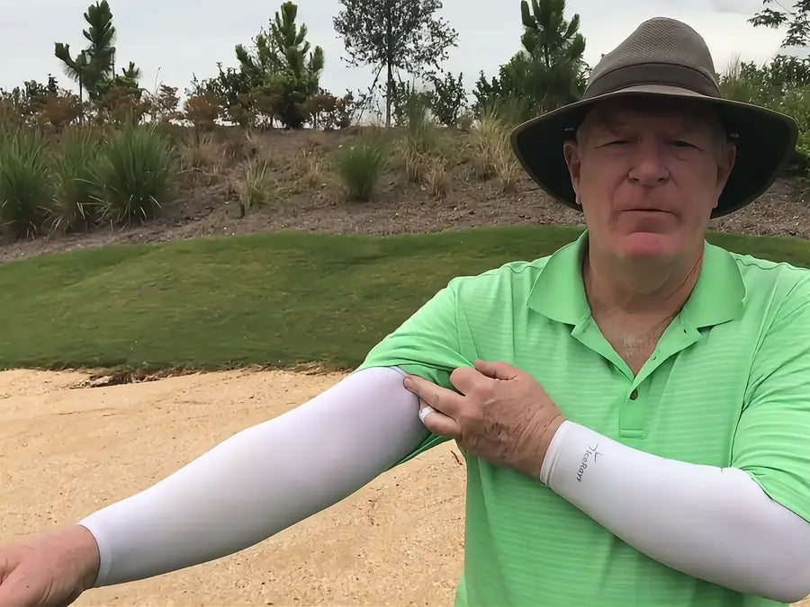 A golfer beside a bunker wearing white IceRays arm sleeves, smooth from wrist to shirt sleeve.
